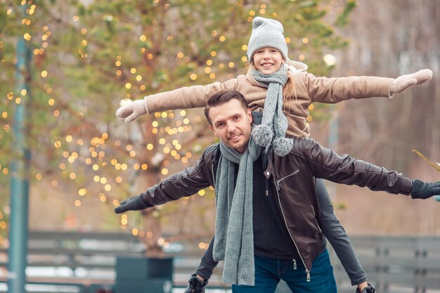 Papá joven y niña adorable se divierten en la pista de patinaje al aire libre