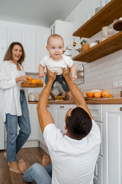 Foto papá está jugando con el bebé en el piso de la cocina, mamá se ríe en el fondo