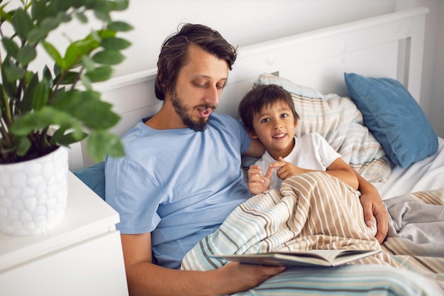 Papá lee un libro acostado en una cama blanca a su hijo antes de irse a la cama