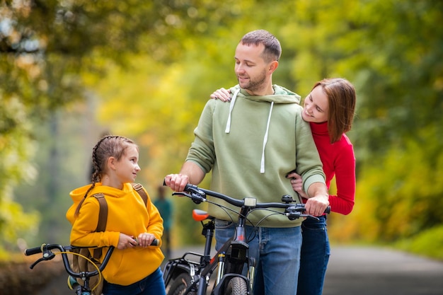 Papá, mamá e hija caminan con sus bicicletas por el camino otoñal del parque