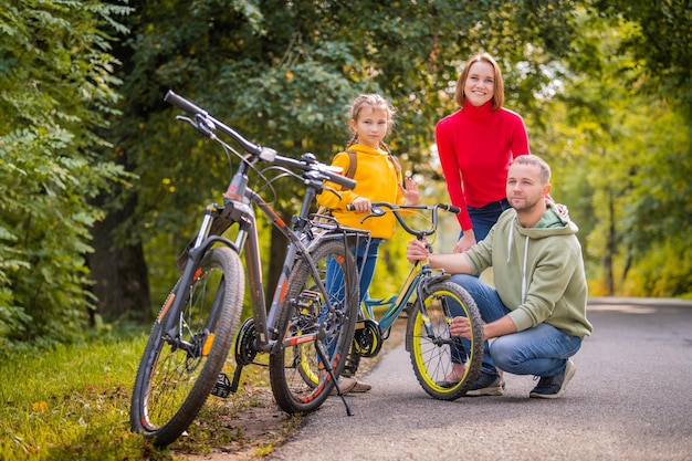 Papá, mamá e hija caminan con sus bicicletas por el camino otoñal del parque