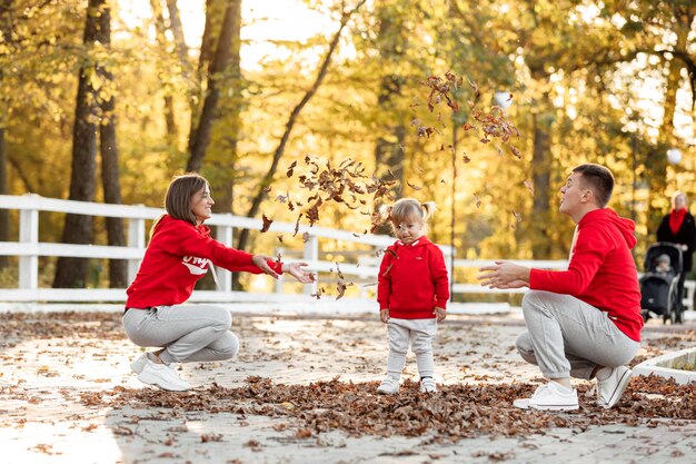 Papá, mamá e hija linda divirtiéndose y jugando con hojas en el parque de otoño.