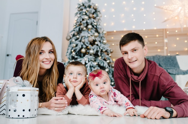 Papá, mamá, pequeño hijo e hija con regalos en el piso cerca del árbol de Navidad