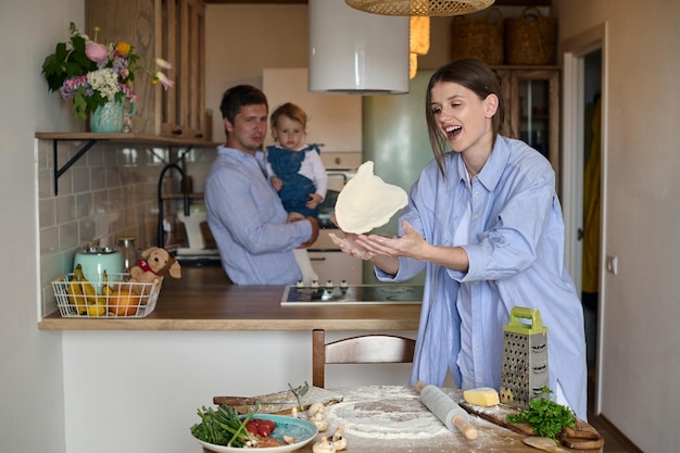 Papá mamá y su hija cocinan pizza juntos en la cocina T