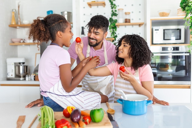 Papá mamá y su pequeña hija cocinan salsa boloñesa para espagueti en la cocina hay vapor escapando de la sartén en el plato de cocina