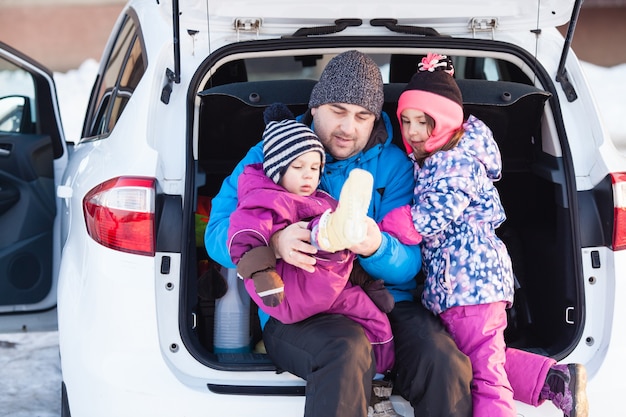 Papa mit Kindern, die im Kofferraum des Autos sitzen und sich auf das Skifahren vorbereiten