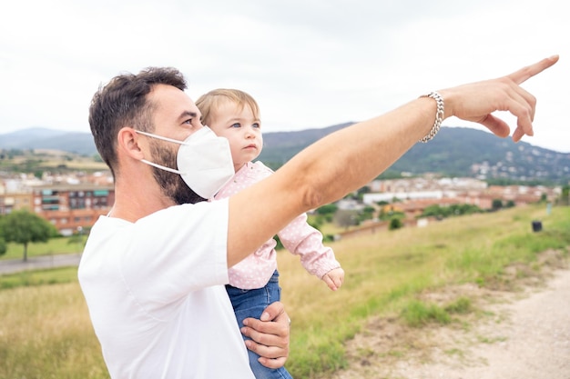 Papa mit Maske, die nach vorne zeigt, während er ein kleines Mädchen hält