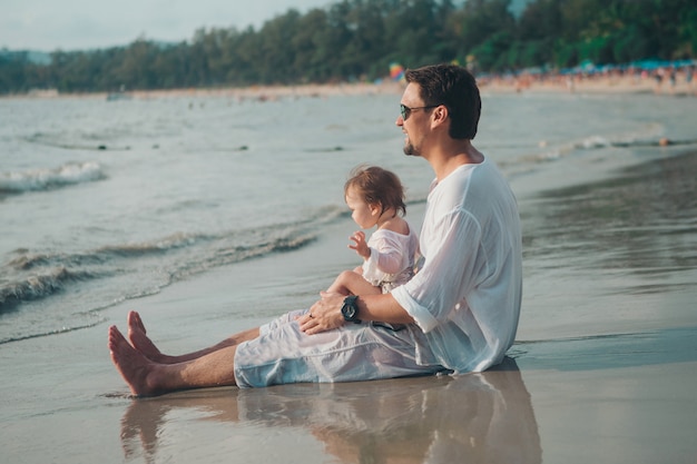 Papa mit Sonnenbrille hält das Baby am Strand in den Armen. Das Konzept der Erziehung des Vaters von kleinen Kindern, Happy Kindheit, eine freundliche Familie.