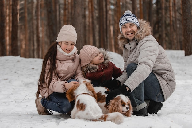 Papa mit Töchtern und Hunden spazieren und spielen im Familienzeitvertreib im Winterwald