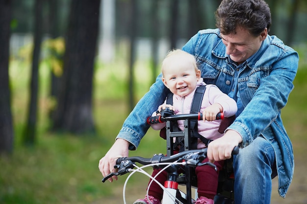 Papá y un niño pequeño andan en bicicleta en verano por el bosque usando una silla de bicicleta para niños