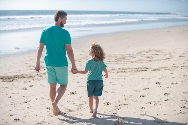 Papá y niño tomados de la mano y caminan juntos padre e hijo caminando en la playa de verano concepto de