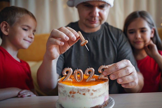 Papá con niños antes de pastel de navidad con números fondo festivo de celebración de año nuevo familiar