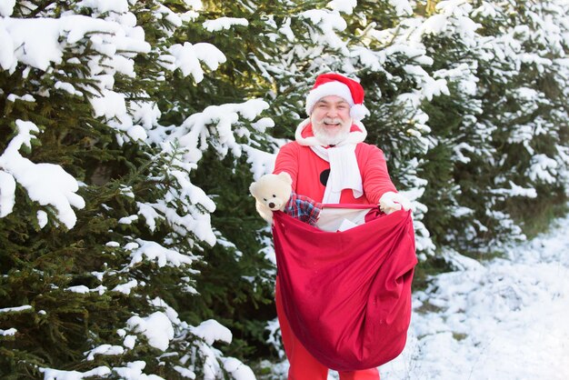 Papá Noel con una bolsa de regalos de Navidad llegando al paisaje nevado del bosque de invierno