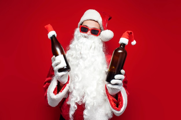 Papá Noel borracho con sombrero y copas festivas bebe vino de una botella de fondo rojo