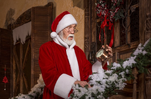 Papá Noel con la cara sorprendida y conmocionada en el porche de la casa de madera decorada.