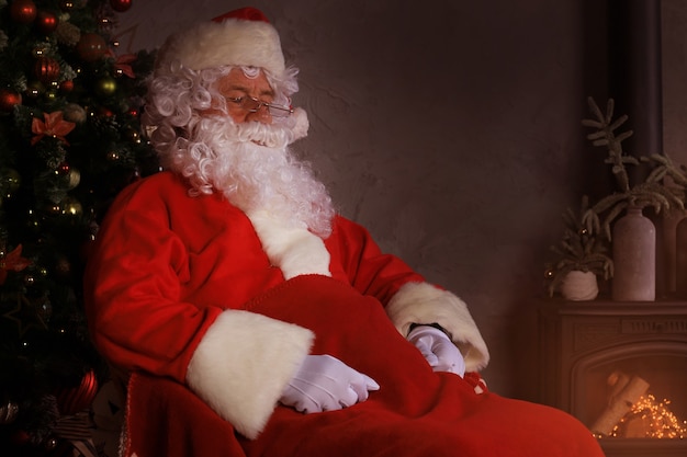 Papá Noel descansando en una cómoda silla cerca de la chimenea en casa.