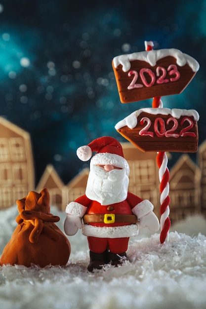 Papá Noel está parado cerca del cartel 2023 en un pueblo nevado