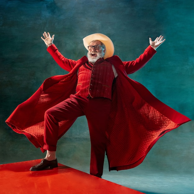 Papá Noel con estilo moderno en traje rojo de moda y sombrero de vaquero sobre fondo oscuro