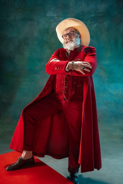 Papá Noel con estilo moderno en traje rojo de moda y sombrero de vaquero sobre fondo oscuro