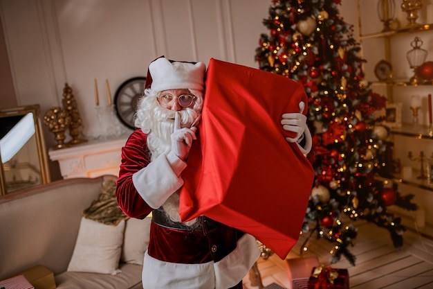 Papá Noel con una gran bolsa roja de regalos se apresura a llevar presente a los niños. Año nuevo y feliz Navidad, felices fiestas concepto