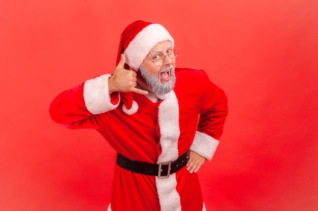 Papá Noel haciendo gesto de teléfono cerca de la oreja y mirando a cámara con la boca abierta.