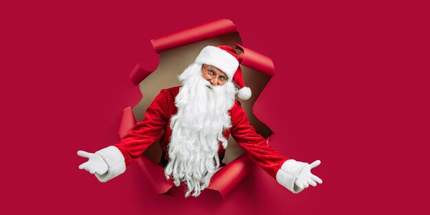 Papá Noel mirando a través del agujero en papel rojo mientras gesticula con las manos como anuncio de bienvenida de Año Nuevo