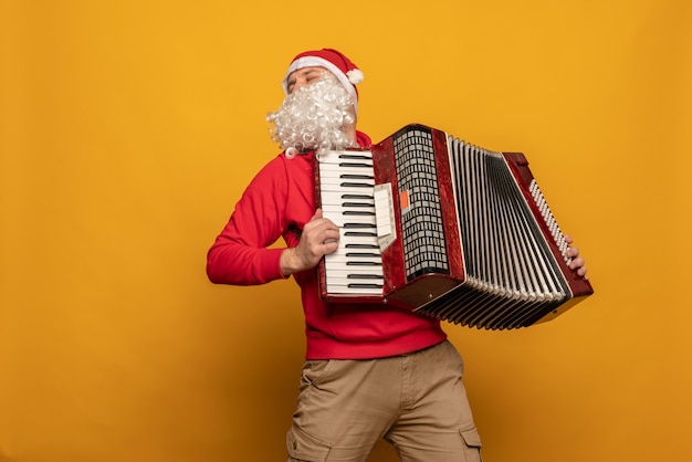 Foto papá noel moderno tocar acordeón emocionalmente aislado sobre fondo amarillo