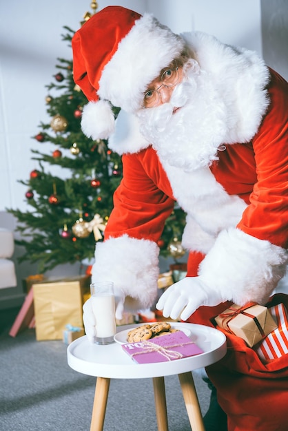 Papá Noel robando galletas y un vaso de leche de la mesa