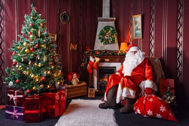 Foto papá noel sentado junto a un árbol de navidad