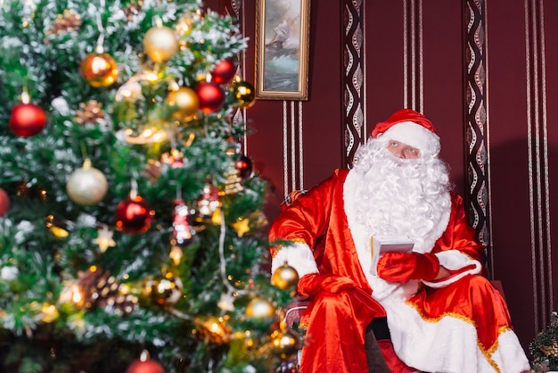 Foto papá noel sentado junto a un árbol de navidad