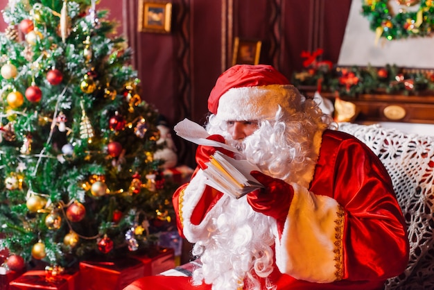 Foto papá noel sentado junto a un árbol de navidad