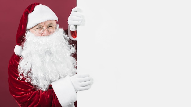 Foto papá noel en el sombrero mirando por la pared blanca