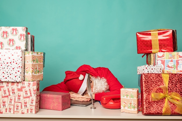 Papá Noel con sombrero trabaja en su oficina con regalos, preparándose para las vacaciones.