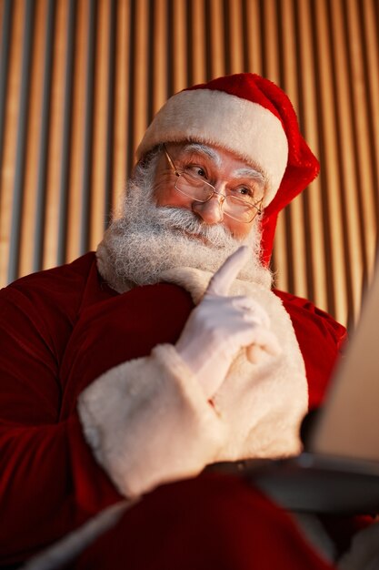 Papá Noel sonriente mostrando el dedo índice mientras habla a través de chat de video en tableta