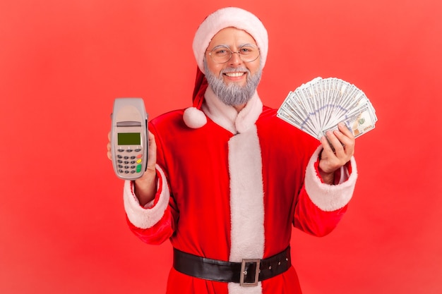 Papá Noel sosteniendo en manos billetes de dólares y terminal, pago sin contacto.