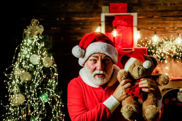 Papá Noel sostiene un juguete de peluche Feliz Papá Noel abraza a un oso de peluche Hombre barbudo en traje de Papá Noel