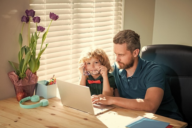 Papá ocupado ayudando a su hijo de la escuela con gafas a estudiar con una computadora en casa nerd