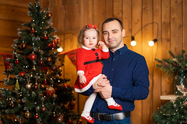 Papá orgulloso decora el árbol de Navidad mientras sostiene a su pequeña hija en sus brazos