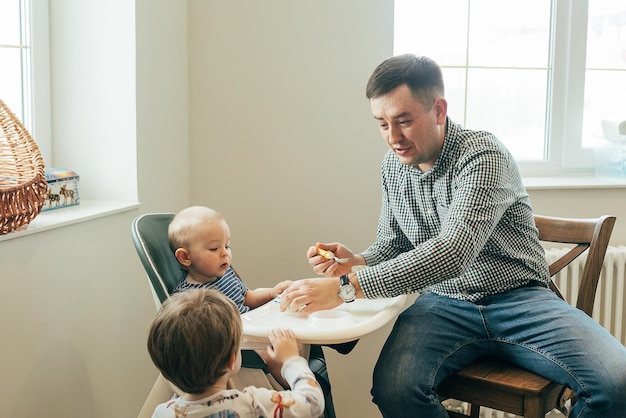 Papá padre alimentando a un bebé lindo con puré en casa sentado en una trona Concepto de alimentación familiar
