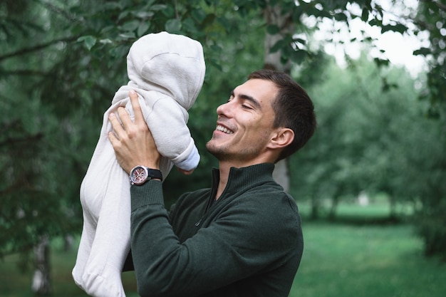 Papá de pelo oscuro en chaqueta verde con bebé infantil en manos