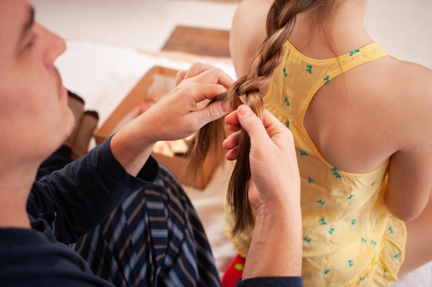 Papá en pijama trenza la coleta de su hija por la mañana