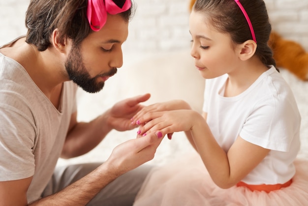 Papá pinta uñas de pequeñas hijas con un esmalte.