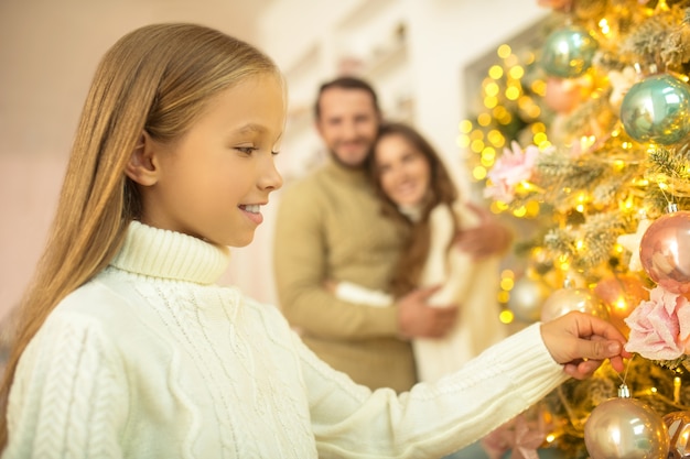 Papá poniendo bolas en el árbol de Navidad mientras su esposa e hija lo miran