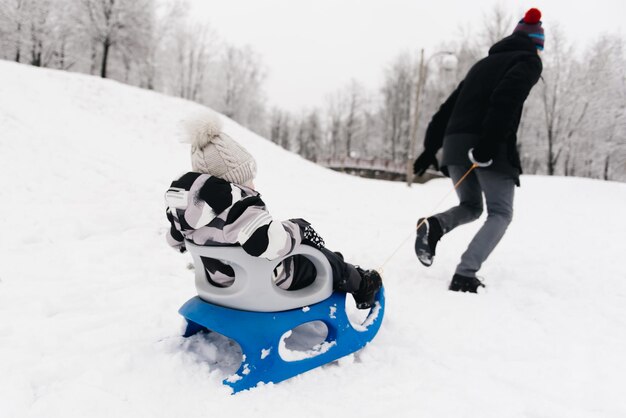 Papa reitet einen süßen Jungen in einem Schlitten in der schneeaktiven Lifestyle-Winterfamilie