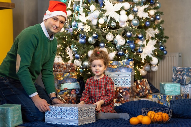 Foto papá con sombrero de santa dando lindo regalo hija para año nuevo. padre con hijo en navidad.