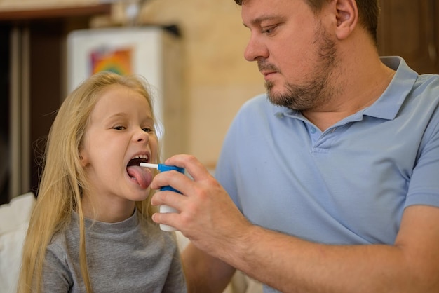 Papa spritzt seinem kranken Kind auf der heimischen Couch Medizin in den Rachen