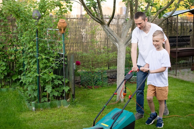 Papá y su curioso hijo cortan el césped verde cerca de la casa.