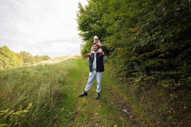 Papá con su hija sobre sus hombros caminando en el bosque