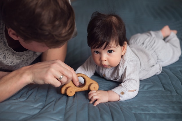 Foto papá y su pequeño hijo se acuestan en la cama y juegan con un coche de madera de juguete