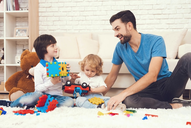 Papá y sus dos hijos juegan juguetes en casa.